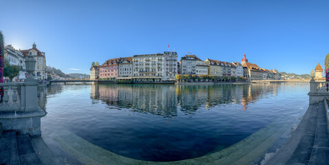 Fototapeta premium Panoramic view of Lucerne's historic cityscape reflected in the Reuss River on a clear day