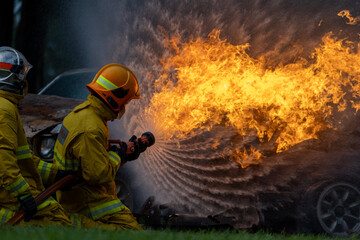 Naklejka premium Team of firefighter in fireproof clothe are using twirl fog watering hose to put out the burning building with high flame for fire extinguish risk rescue mission, accident management