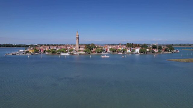 Aerial view of Burano's colorful houses, church bell tower, canals, and Venetian lagoon.