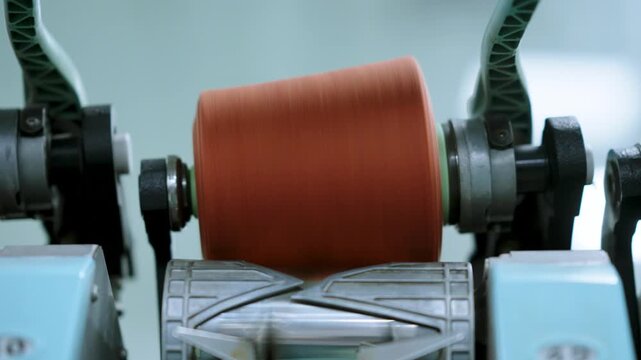 Textile machinery with orange yarn spool winding in close-up detail