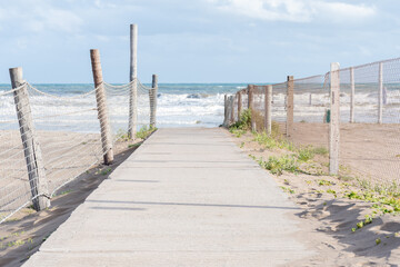 Obraz premium Path to access the beach surrounded by sand and vegetation.