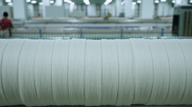 Close-up of large white yarn spool in textile factory workshop with industrial background
