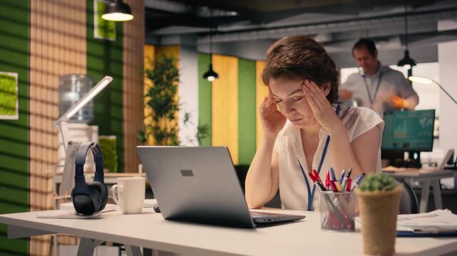 Businesswoman experiencing headache and eye strain working in corporate office, rubbing temples in visible fatigue and stress. Migraine and blurred vision due to work tension, discomfort.