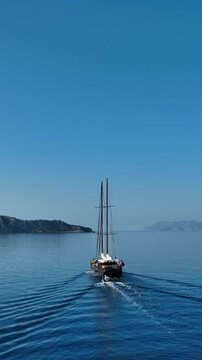 Traditional wooden gulet sailing on calm blue sea with distant islands under clear sky