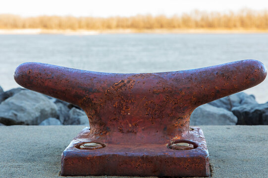 Worn Rusty Mooring Bollard. A weathered, rusty metal bollard is firmly secured on a concrete surface at the Mississippi River Port in Cape Girardeau, a docking site for riverboats