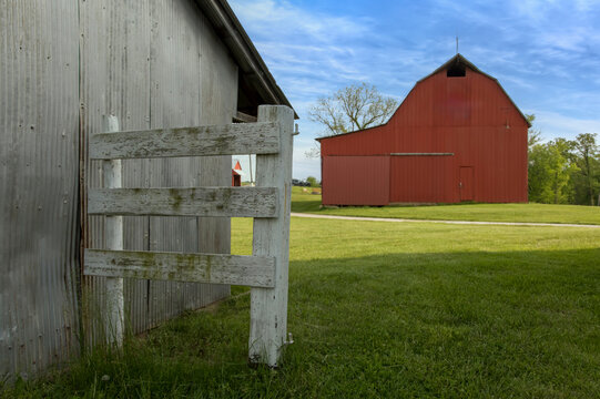 Farm scene with a red barn behind a white fence in bright sunlight 