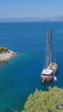 Traditional wooden gulet sailing boat anchored in a tranquil turquoise bay with distant mountains
