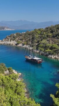 Traditional wooden gulet sailing in a secluded turquoise bay surrounded by lush green hills and mountains