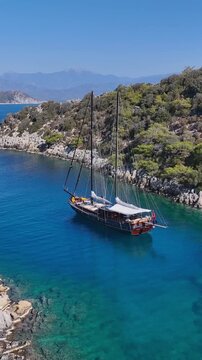Traditional wooden gulet sailing boat anchored in a secluded turquoise bay with lush green hills