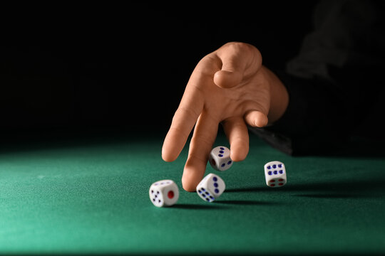 Male hand throwing white game dices on green table against black background