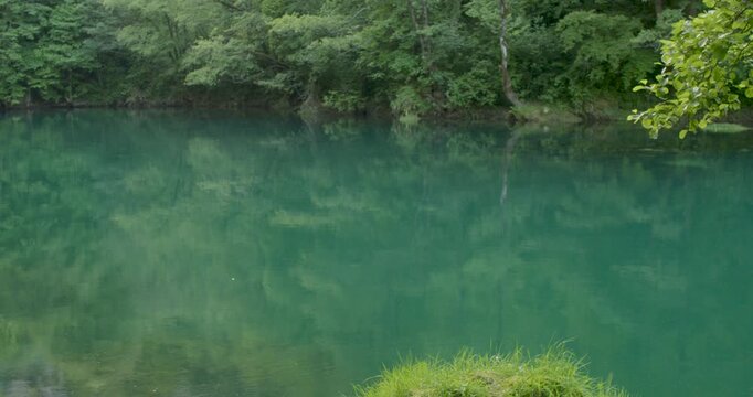 Ultra clear emerald water of the Una River reflecting dense green forest in Bosnia and Herzegovina. Calm turquoise surface, pristine Balkan wilderness landscape, tranquil European eco tourism 