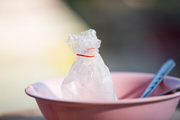 Plastic bag and plastic spoon in pink bowl on blurred background.