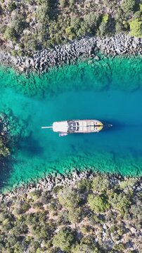 Aerial view of a traditional gulet sailing through crystal clear turquoise waters near a rocky coastline