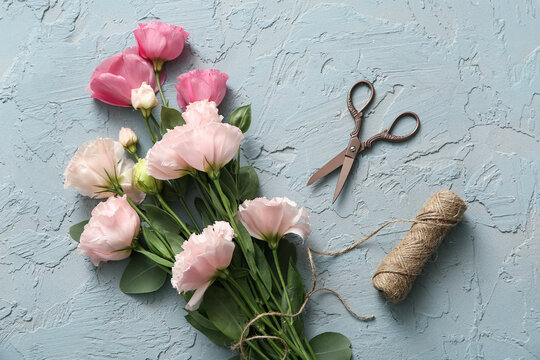 Composition with beautiful eustoma flowers, scissors and threads on blue grunge background