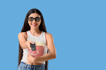 Pretty young woman with remote controller and popcorn on blue background