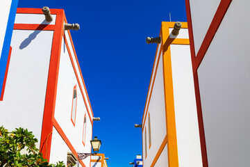 Narrow alley framed by trimmed buildings. Vintage lamp and greenery add charm to geometric, sunlit scene. Architectural detail of traditional buildings featuring exterior drainage spouts protruding