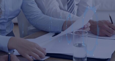 Reviewing two colleagues turning documents and writing on notepad at meeting table, tie, blue HUD