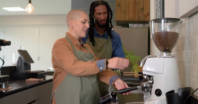 Diverse coworkers pulling lever on grinder, filling portafilter and training at coffee shop counter