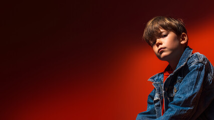 Young boy portrait with serious look wearing denim jacket expressing individuality, emotions, confidence, youth identity, diversity, candid expression. Flat red background. Copy space. Banner template