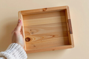 Person holding a handmade wooden tray or empty picture frame on beige background.