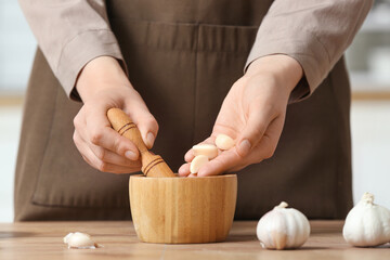 Woman with mortar and garlic at table in kitchen