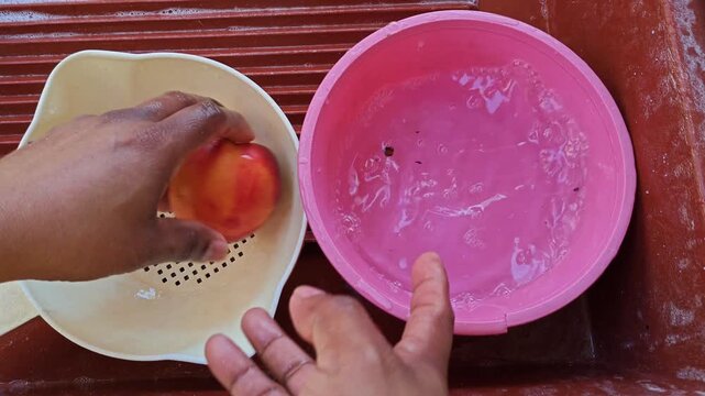 Hands washing a whole fresh nectarine in a purple bowl