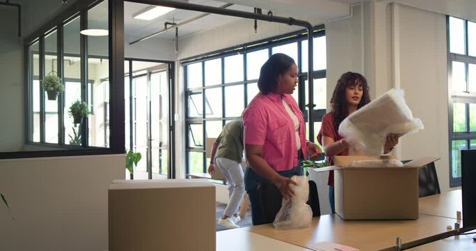African American coworkers opening box, unpacking, pointing and inspecting wrapped item at office