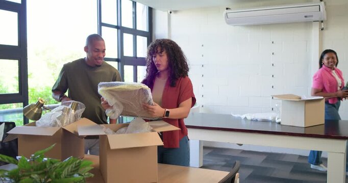 African American coworkers unpacking boxes at office after move, placing plants, lamp, cushion