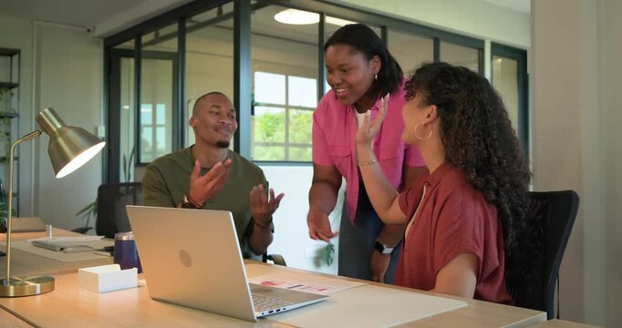 African American coworkers gathering at desk, standing woman pointing at laptop, reviewing charts