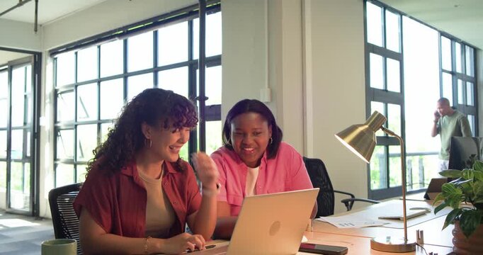 Female coworkers spotting chart on laptop, papers in office, typing and pointing to finalize report