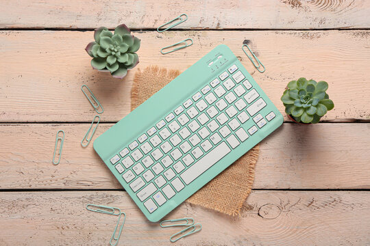 Cyan computer keyboard, clips and houseplants on wooden background