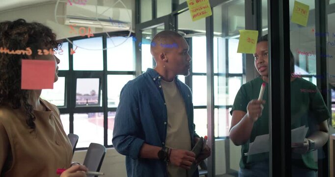 Diverse coworkers brainstorming, left woman placing yellow sticky notes on glass, circling 40%