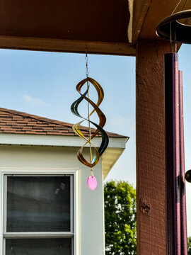 A wind decoration hanging from a porch on a sunny day