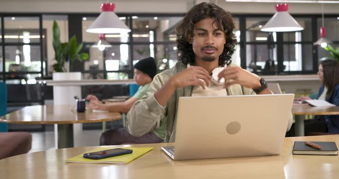 Adult Indian man typing on laptop in coworking area, adjusting for focus, putting on headphones