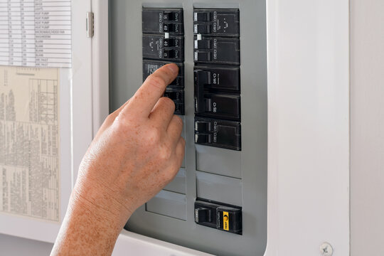 Woman's hand operating a residential electrical panel inside a home. Concept of household electricity, power control, safety, maintenance, and home utilities in a domestic interior