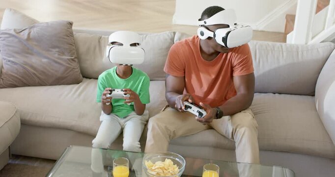 African American father and son playing VR game on couch with headsets on and white controllers