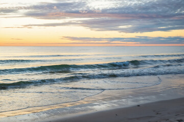 Peaceful ocean waves rolling onto the beach at sunrise, with soft pastel colors reflecting on the water and sand under a calm, serene sky.