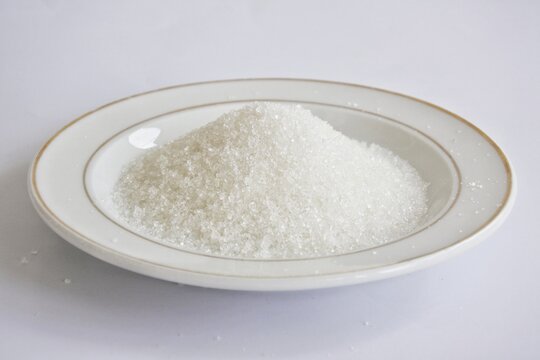 A white ceramic plate is filled with sugar on a white background.