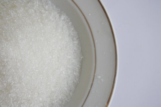 A white plate is filled with sugar on a white background, top view, half photography with negative space. 