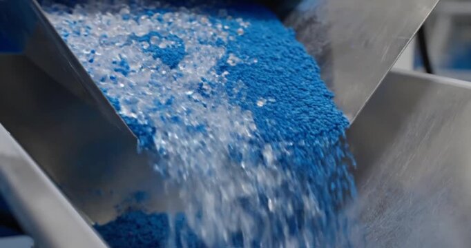 Blue granules being poured from a metal chute.