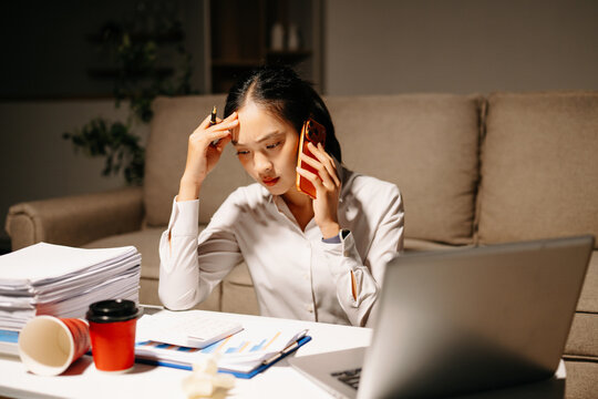 Stressed businesswoman talking on phone while working late with laptop and paperwork. Deadline pressure, finance problems, overtime