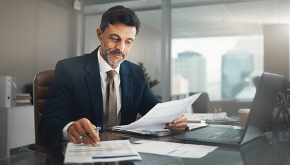 Obraz premium Entrepreneur reviewing financial documents at office desk with laptop and papers
