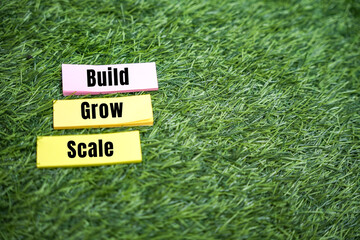 Build grow scale written on sticker over green grass background for startup and business growth strategy concept.