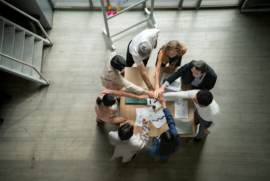 Top view of a multicultural business team stacking hands together over a meeting table, symbolizing unity
