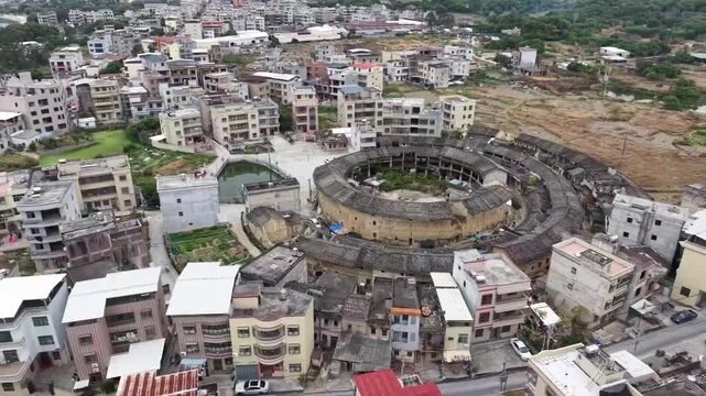 A stunning 1080p horizontal aerial shot of the Fujian Tulou, a UNESCO World Heritage site. The footage captures the unique circular and square earthen structures nestled among lush green mountains, sh