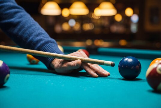 Male hand holding wooden cue stick aiming at blue ball on teal billiard table in dimly lit pub