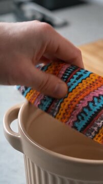 A hand sealing a large food container with a patterned beeswax wrap, showing the flexibility and texture of the eco-friendly alternative to cling film.. Zero-Waste Lifestyle & Sustainable Packaging.
