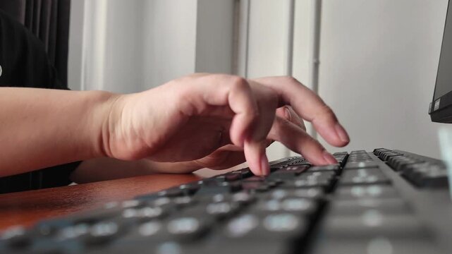 A side-view close-up of man's hands typing on computer keyboard on desk inside an office building. Horizontal footage, normal motion, 4K resolution