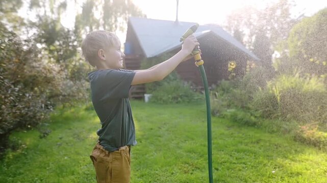 Funny boy pouring cool water on himself and playing with garden hose with sprinkler in sunny backyard on hot summer day. Happy child having fun with water splashes. Summer outdoor activity for kids.