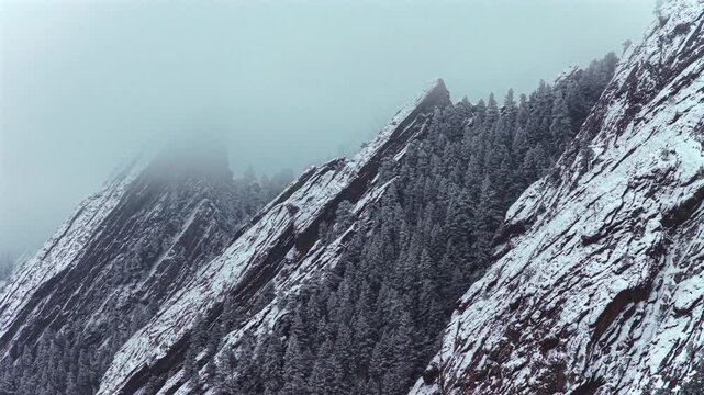 Winter snowing lightly fog Flat Irons rock formations slabs Chautauqua Park trail aerial drone Boulder Colorado sunset dusk evening snowy trees snow falling foggy grey skies low cloud layer forward